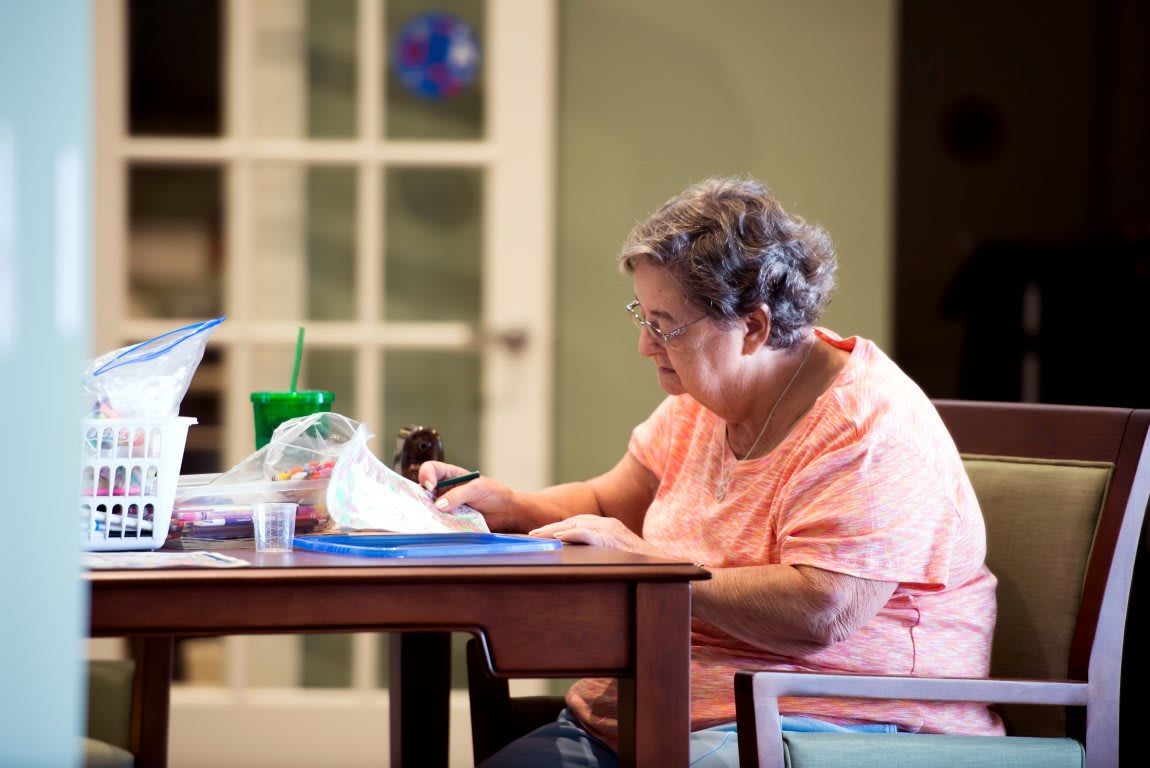 An elderly woman sitting at a table, reading a book indoors.