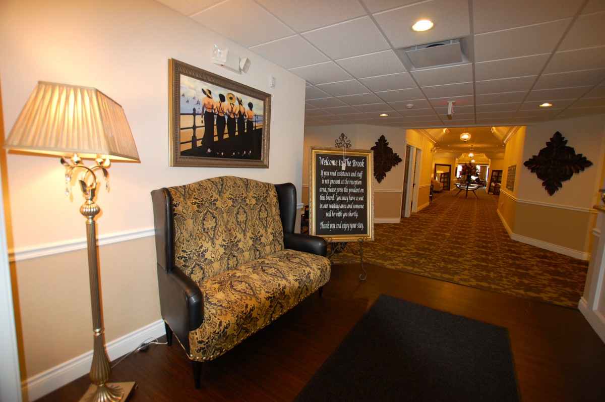 A well-decorated hallway with a patterned sofa, framed artwork, and a lamp, featuring a signboard in front.