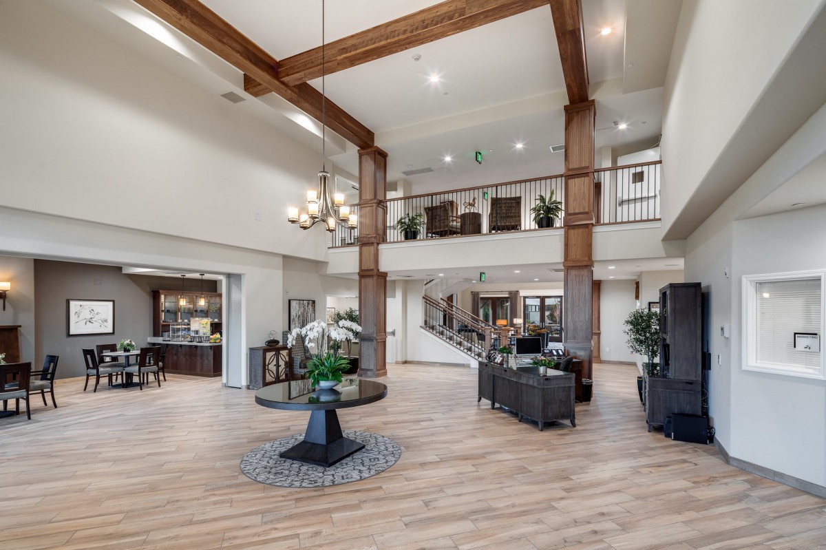 A spacious and modern lobby featuring a chandelier, wood beams, and comfortable seating.