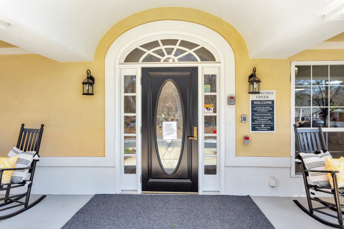 A symmetrical building entrance with a black door and arched window design, flanked by lantern-style lights on a yellow wall.