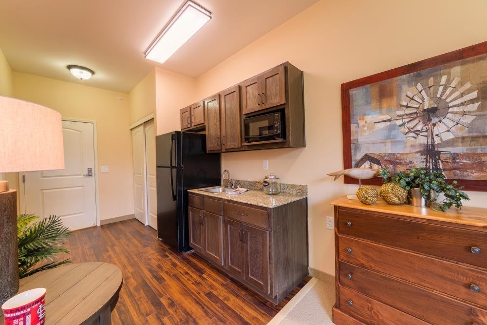 A small kitchen area with wooden cabinets, a black refrigerator, and a microwave.