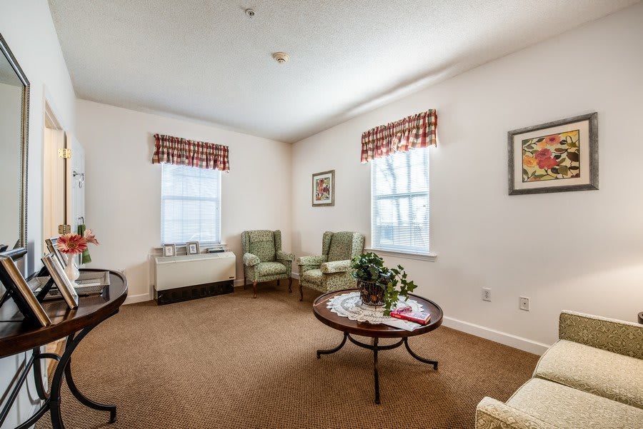 A cozy living room with two armchairs, a round coffee table, and natural lighting from the windows.