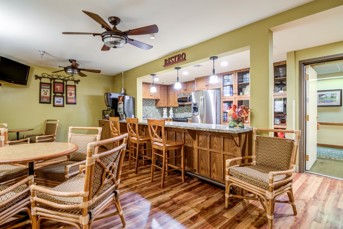 A modern kitchen and dining area featuring wooden flooring, bar stools, ceiling fans, and warm indoor lighting.