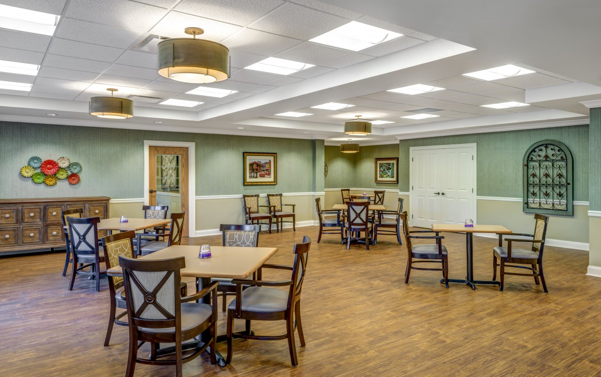 A spacious and well-lit dining room with multiple tables and chairs, featuring elegant lighting fixtures and wooden flooring.