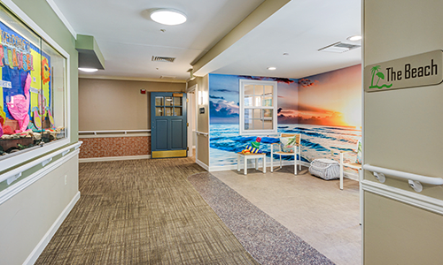 A waiting area with a beach mural and sunset, featuring chairs and a carpeted floor.