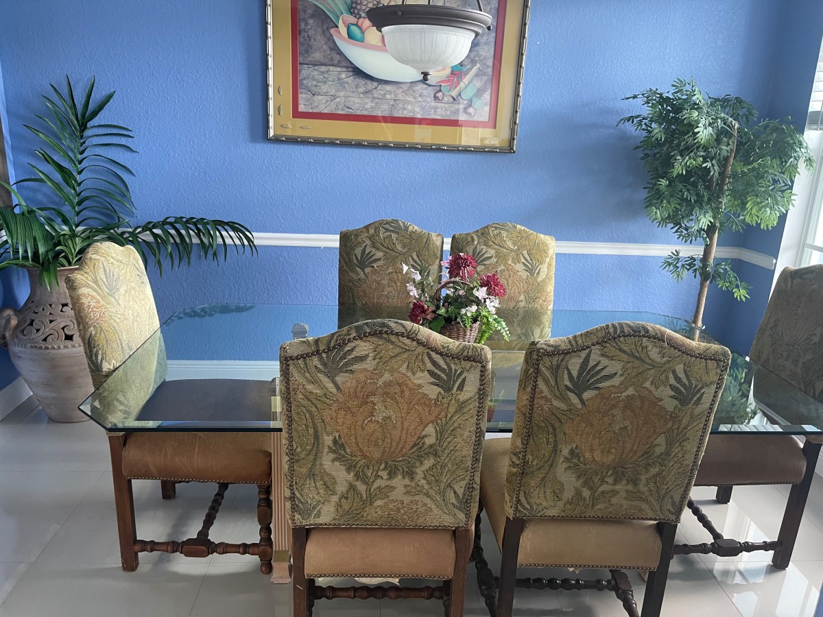 A dining room with an elegant table set, ornate chairs, and decorative elements including a framed painting and indoor plants.