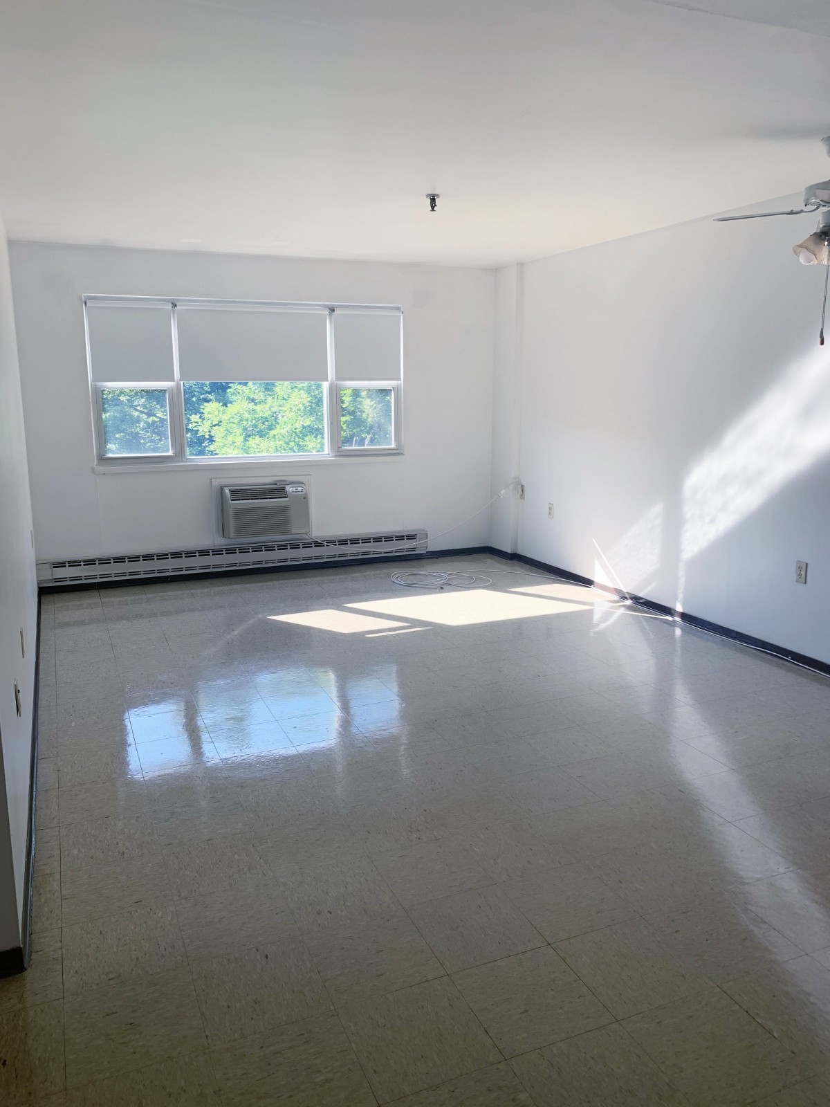 A bright, empty room with white walls and large windows allowing natural light in.