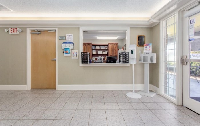 A well-lit reception area with a counter, sanitizer station, and tiled flooring.