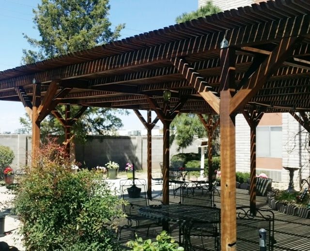 A wooden pergola providing shade over a patio area in a landscaped garden.