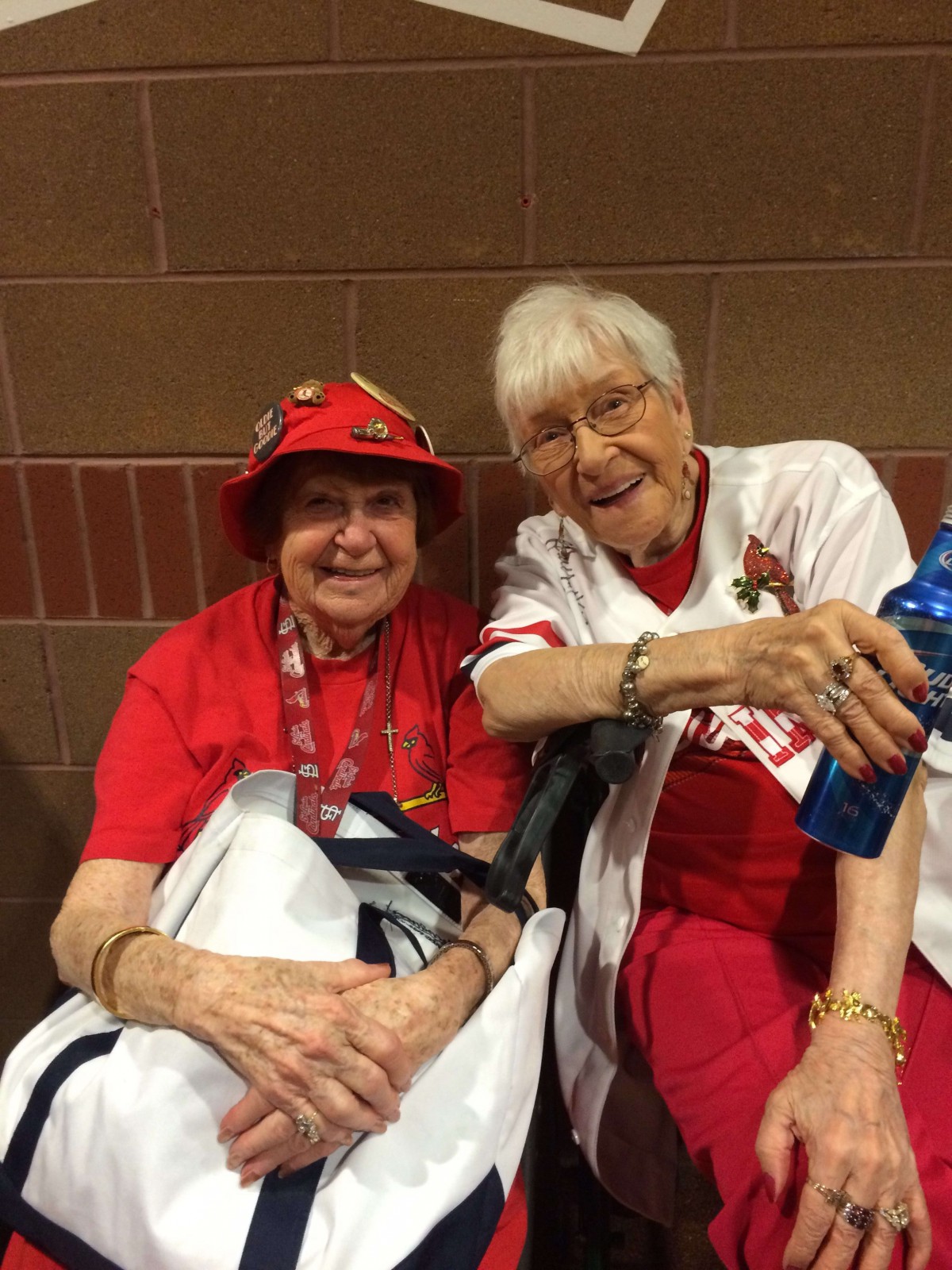 Two elderly women enjoying a sports game, dressed in team colors and smiling cheerfully.