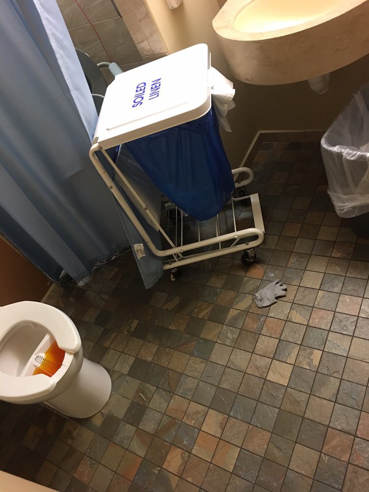 A bathroom with a toilet, trash bin, and cleaning supplies.