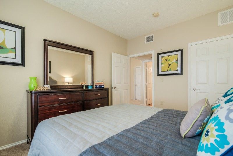 A cozy bedroom with a neatly made bed, a large dresser topped with a mirror, and artwork on the walls.