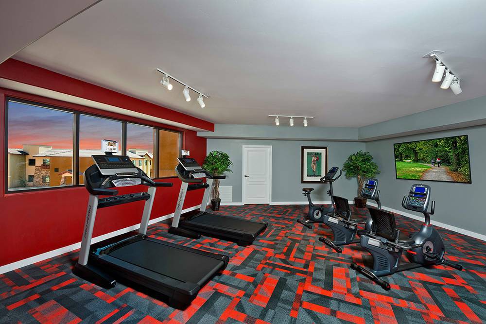 A well-equipped indoor gym with treadmills, stationary bikes, and vibrant red walls.