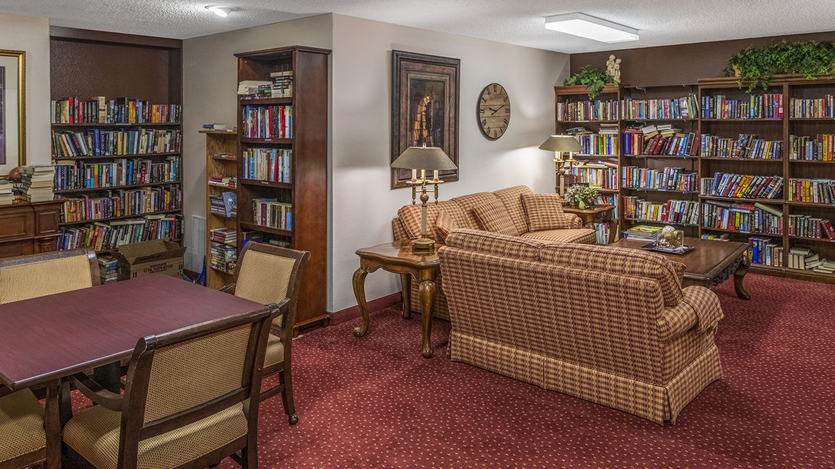 A cozy library room with a sofa, chairs, and shelves filled with books.