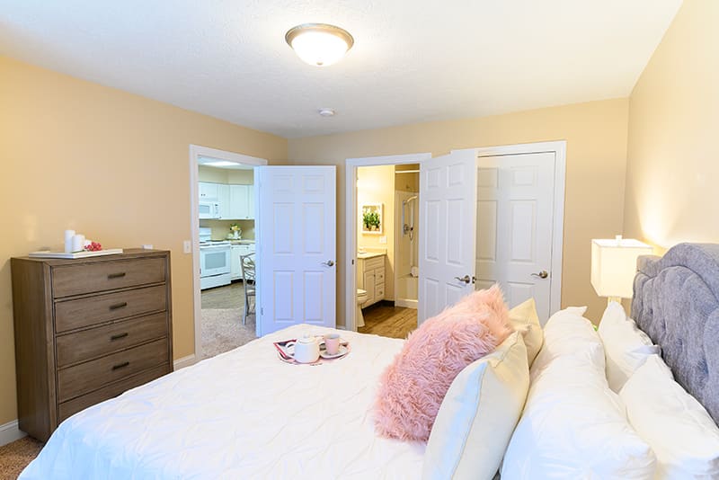 A cozy bedroom with a neatly made bed, pink pillows, and open doors leading to other rooms.