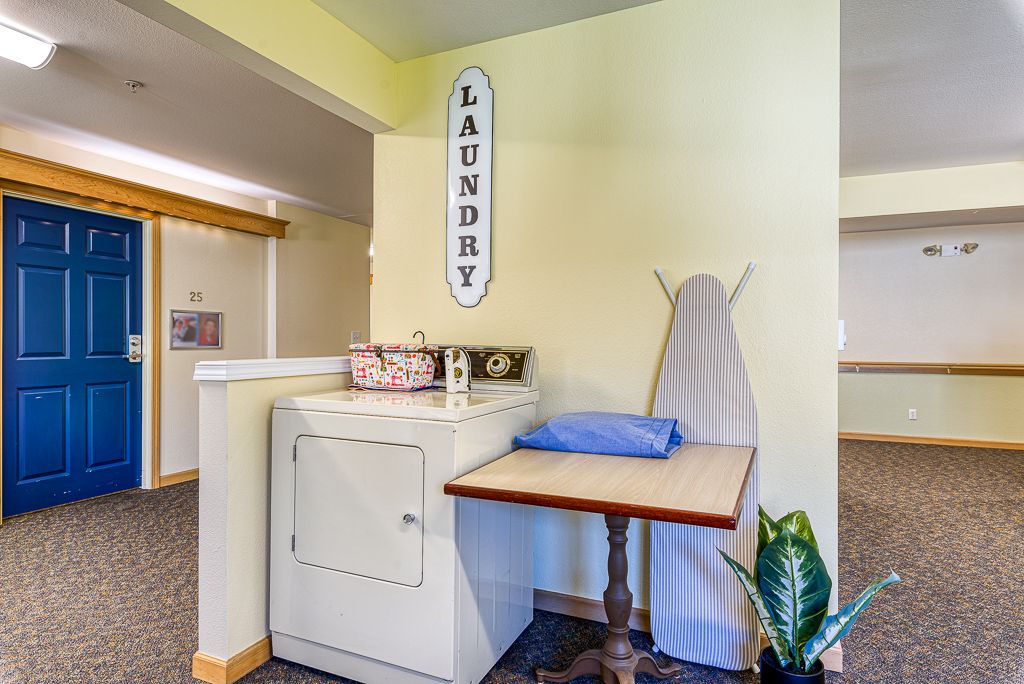 A cozy laundry room with a washing machine, ironing board, and a decorative 'Laundry' sign on the wall.