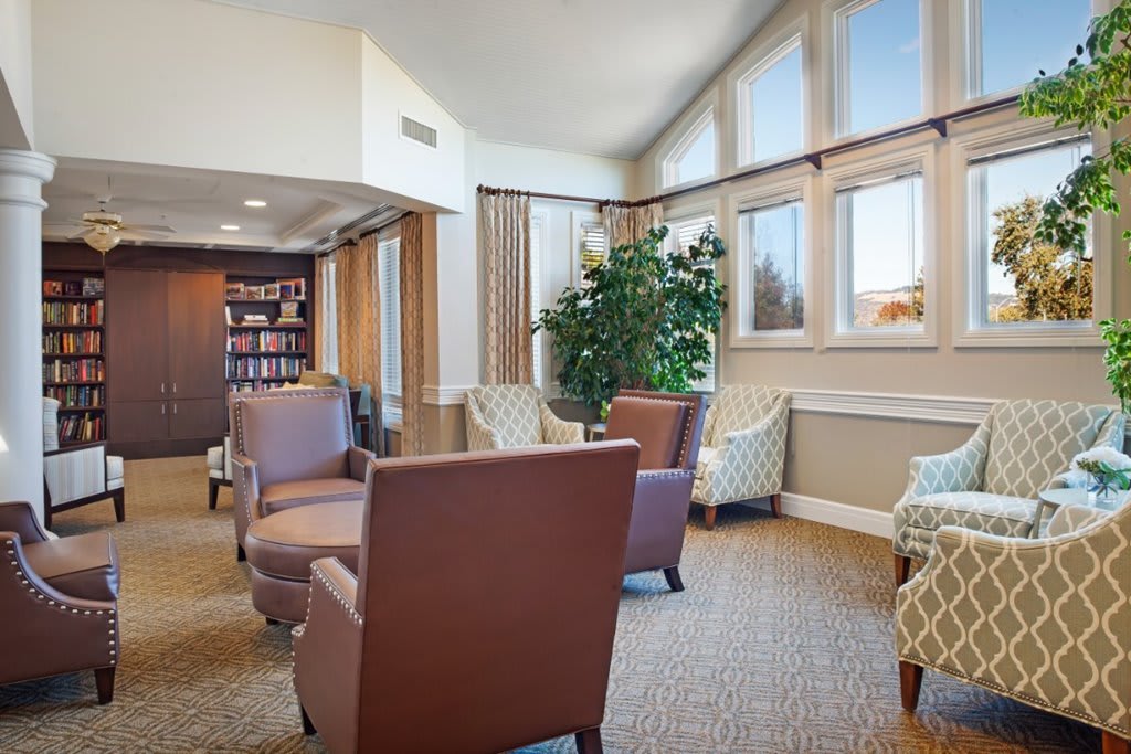 A cozy living room with comfortable seating, large windows, and a bookshelf.