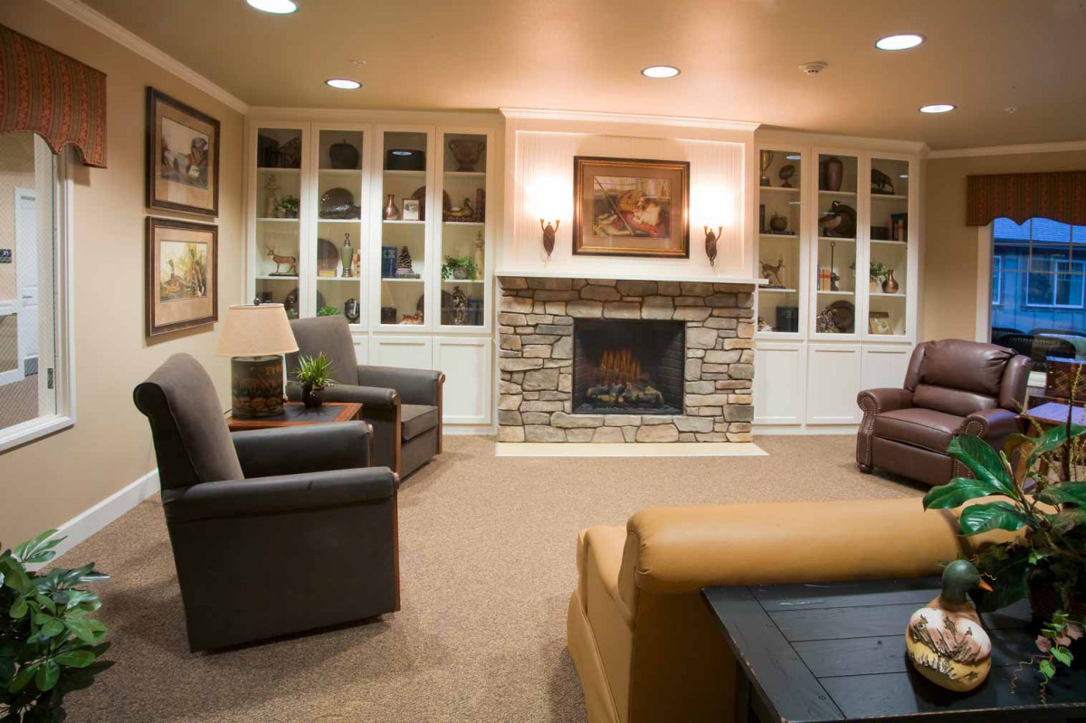 A cozy living room with a stone fireplace, surrounded by comfortable armchairs and built-in bookshelves.