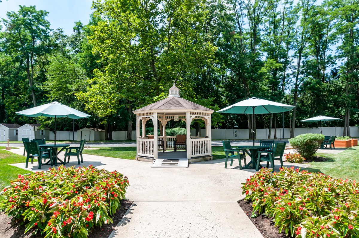 A peaceful garden with a central gazebo and surrounding tables with umbrellas.