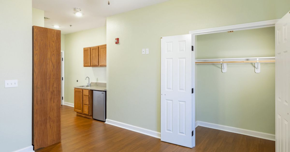 A small kitchenette in an apartment with wood flooring, featuring a closet and cabinets.