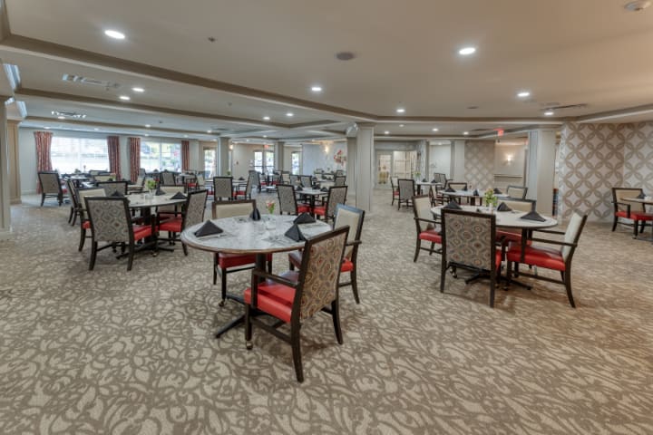 Spacious dining area with multiple tables and chairs, featuring elegant carpeting and soft lighting.