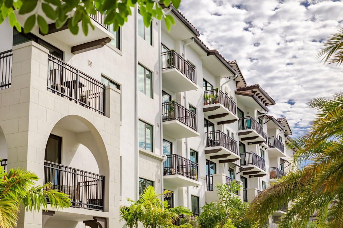 A modern apartment building with multiple balconies surrounded by greenery.