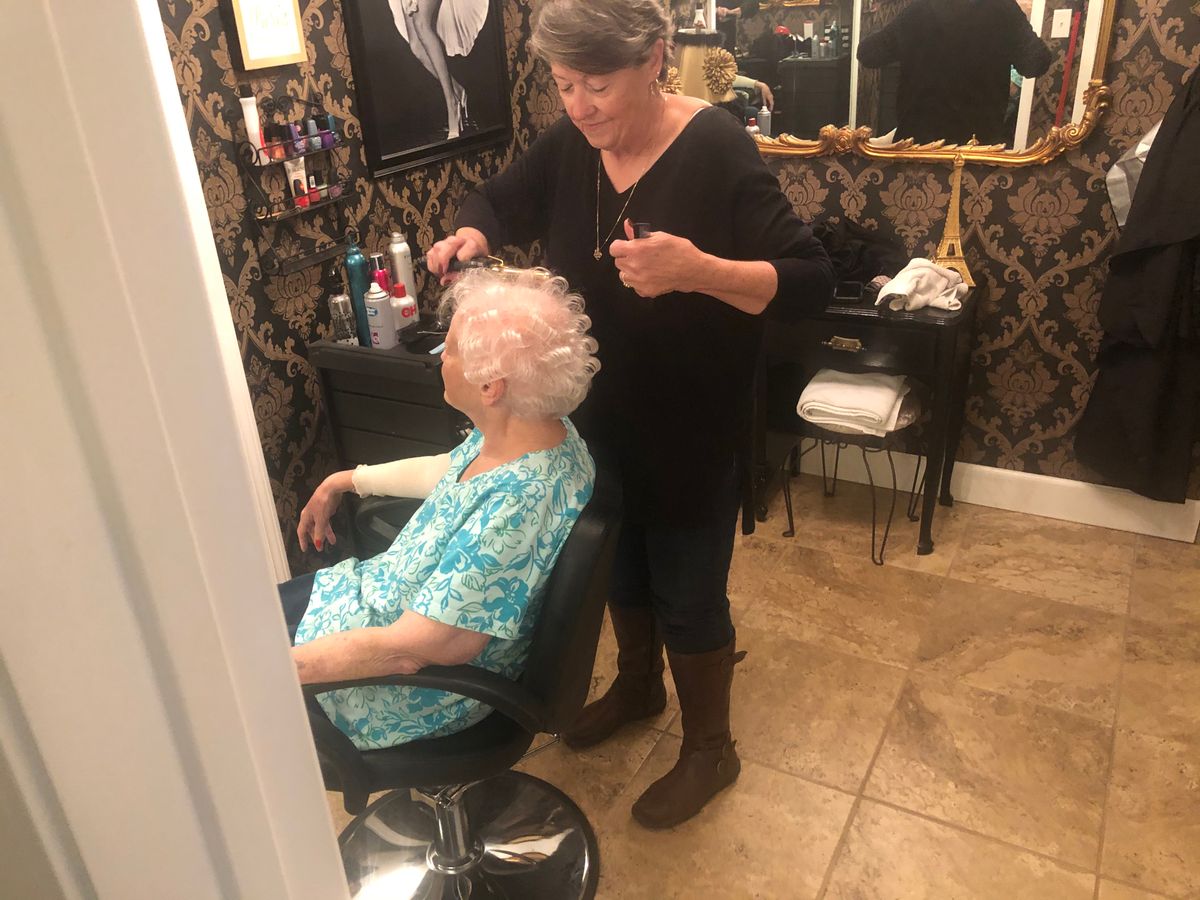 A hairdresser styles the hair of a senior woman in a salon.