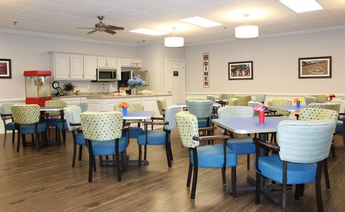 A modern dining area with a kitchen, featuring colorful chairs and tables in a community setting.