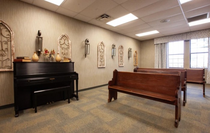 A small chapel with wooden pews, a piano, and religious decorations on the wall.
