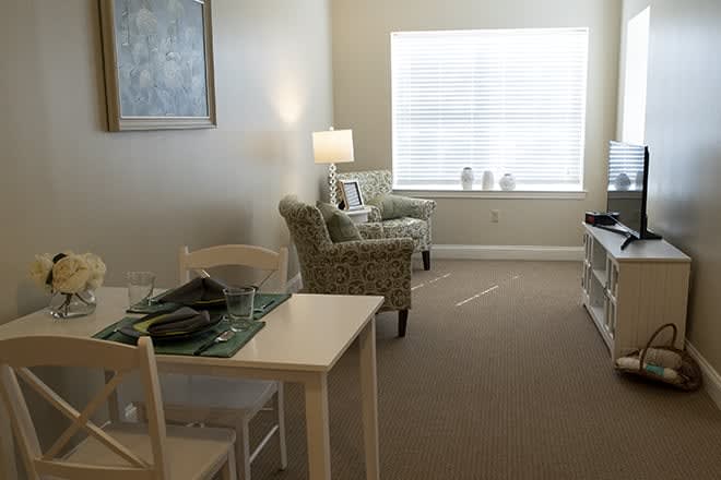 A cozy living room with a small dining table, two chairs, and a lamp by the window.