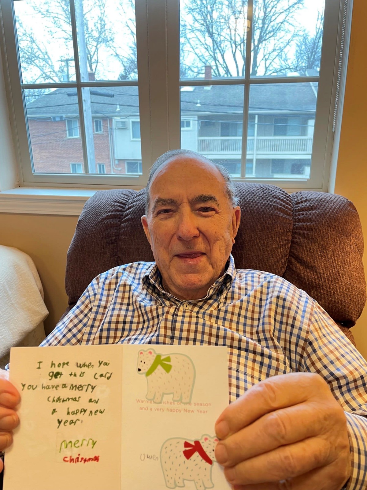 An elderly man sitting in a chair holding a greeting card indoors.