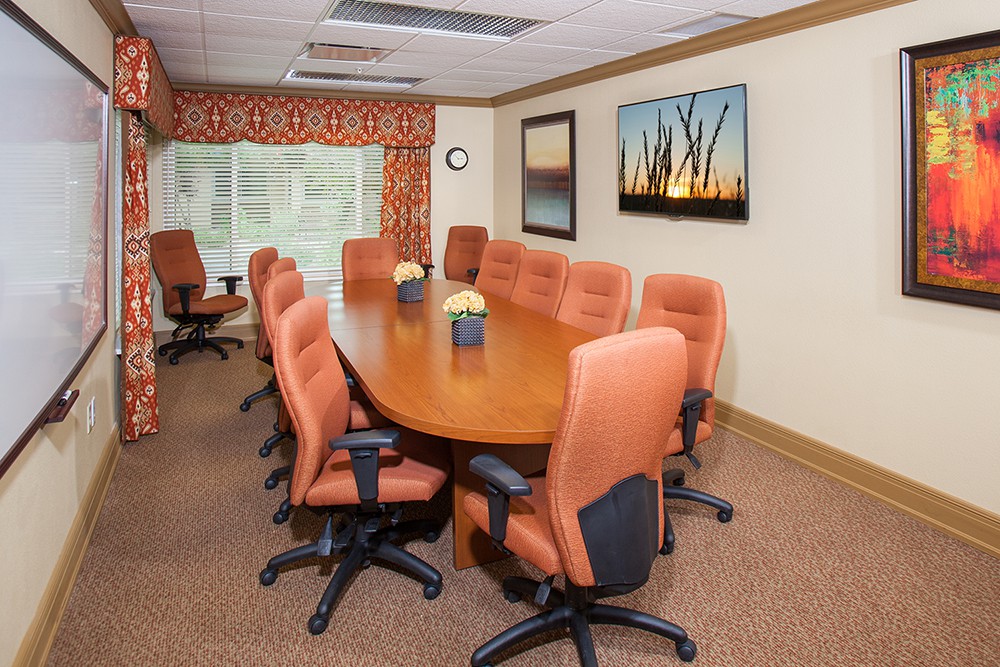 A well-furnished conference room with an oval meeting table and comfortable office chairs, featuring artwork on the wall.