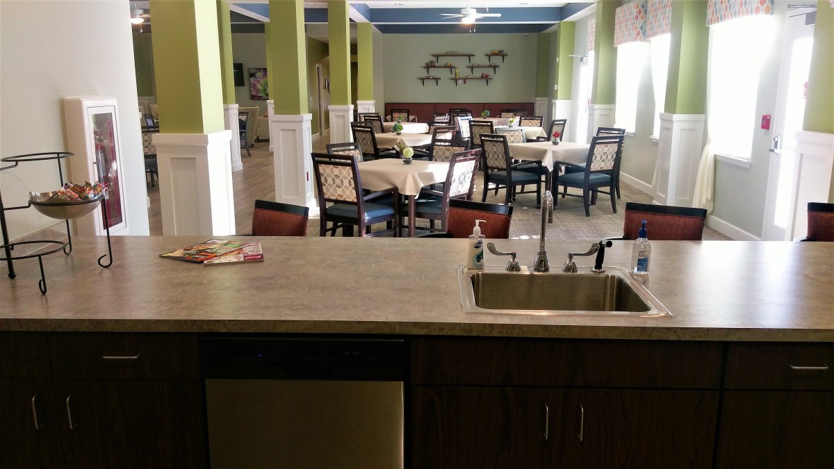 A neatly arranged dining area with multiple tables and chairs, viewed from behind a countertop with a sink.