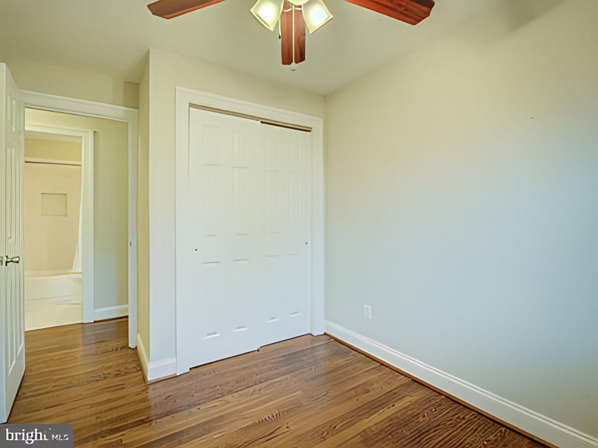 A small empty room with a ceiling fan and hardwood flooring.
