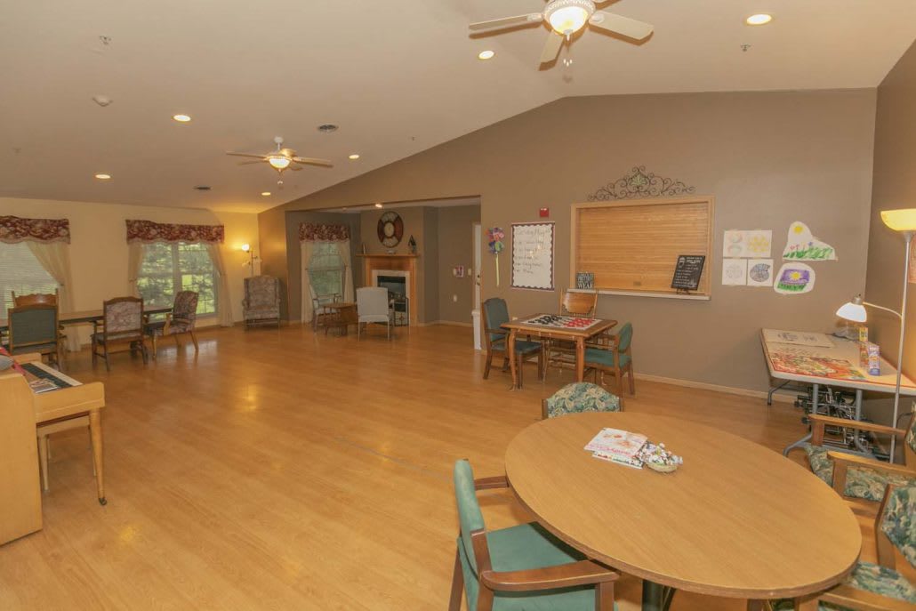 A spacious community room with wooden flooring, tables, and chairs arranged for social gatherings.