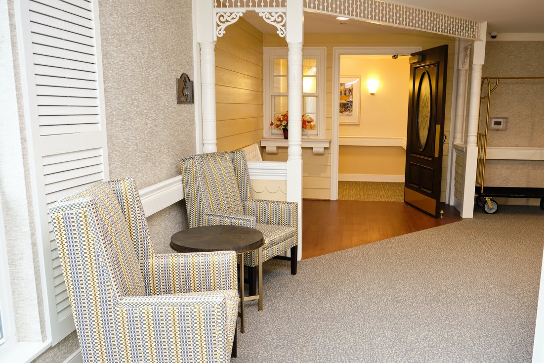 A cozy lobby area with patterned chairs and a small table, leading to a well-lit hallway.