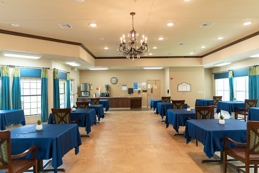 A spacious dining area featuring tables draped in blue tablecloths, illuminated by a chandelier.