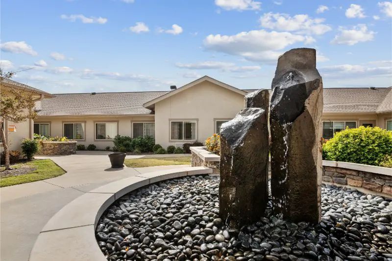 A modern outdoor fountain with large rocks in front of a residential building under a clear sky.