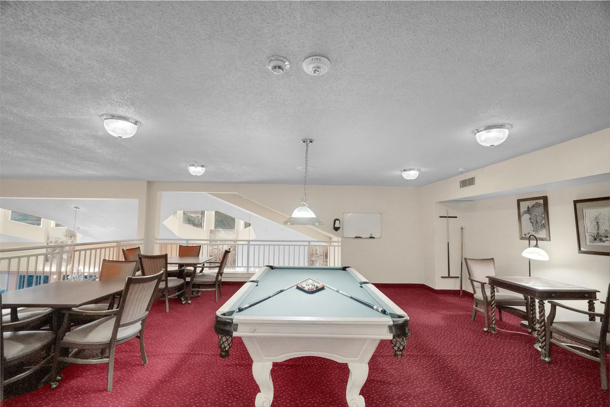 A game room featuring a pool table and seating area on red carpet.