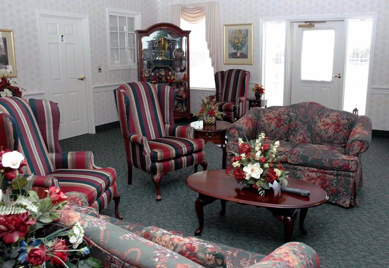 A cozy living room with striped chairs and floral-patterned sofas surrounding a wooden coffee table with decorative flowers.