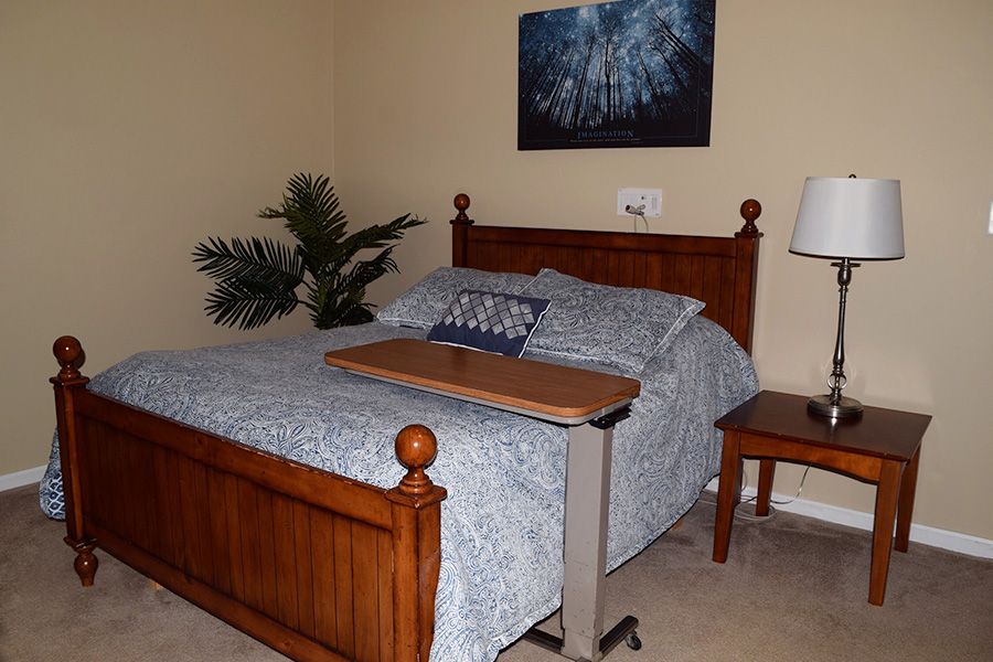 A cozy bedroom with a wooden bed frame, adorned with blue bedding and an adjustable bedside table.