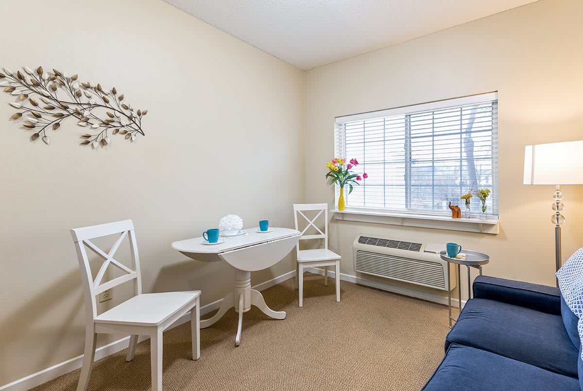 A cozy living room with a small dining table, chairs, and a window with natural light.