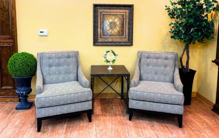 A cozy seating area with two gray armchairs, a small table, and decorative elements in a warmly lit room.