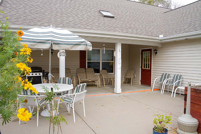 A cozy outdoor patio with chairs, tables, and an umbrella, situated next to a house.