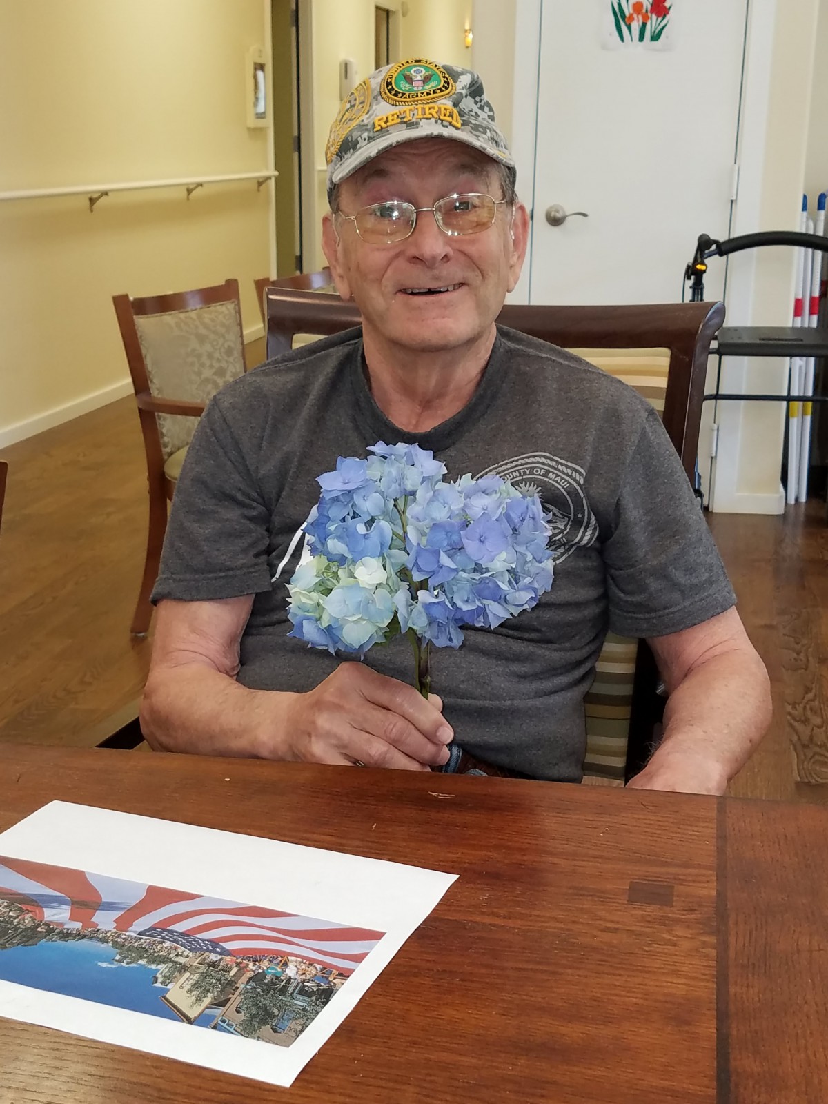 A man sitting at a table holding blue flowers and smiling.