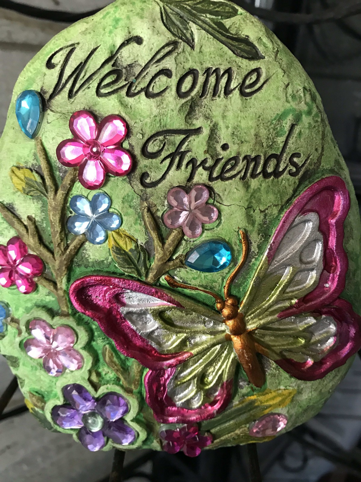 A colorful decorative stone with a butterfly and flowers, featuring the message 'Welcome Friends'.