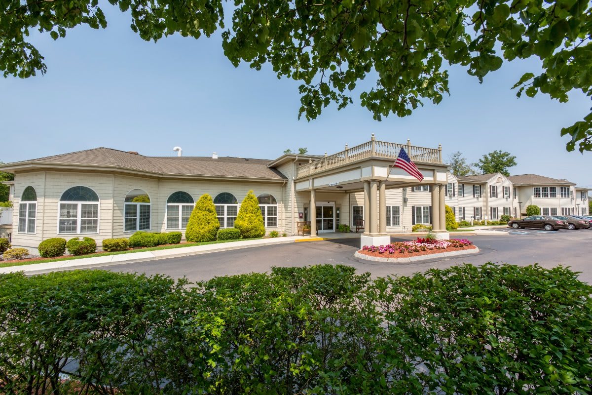 A sunny view of a building entrance with well-maintained landscaping and an American flag.