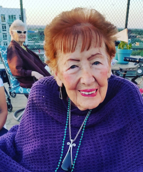Elderly woman enjoying a day outdoors, wearing a purple shawl and smiling warmly.