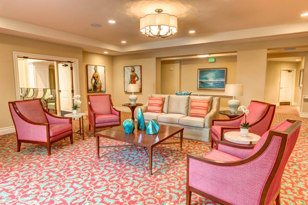 A cozy living room with pink chairs and a patterned rug, accented by modern artwork and elegant lighting.