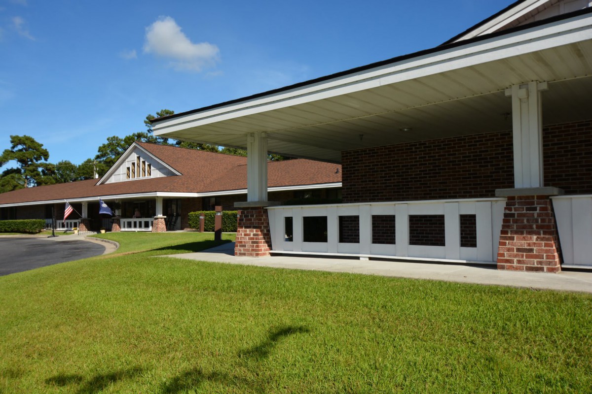 A modern building with a sloped roof and brick accents surrounded by green grass under a clear blue sky.